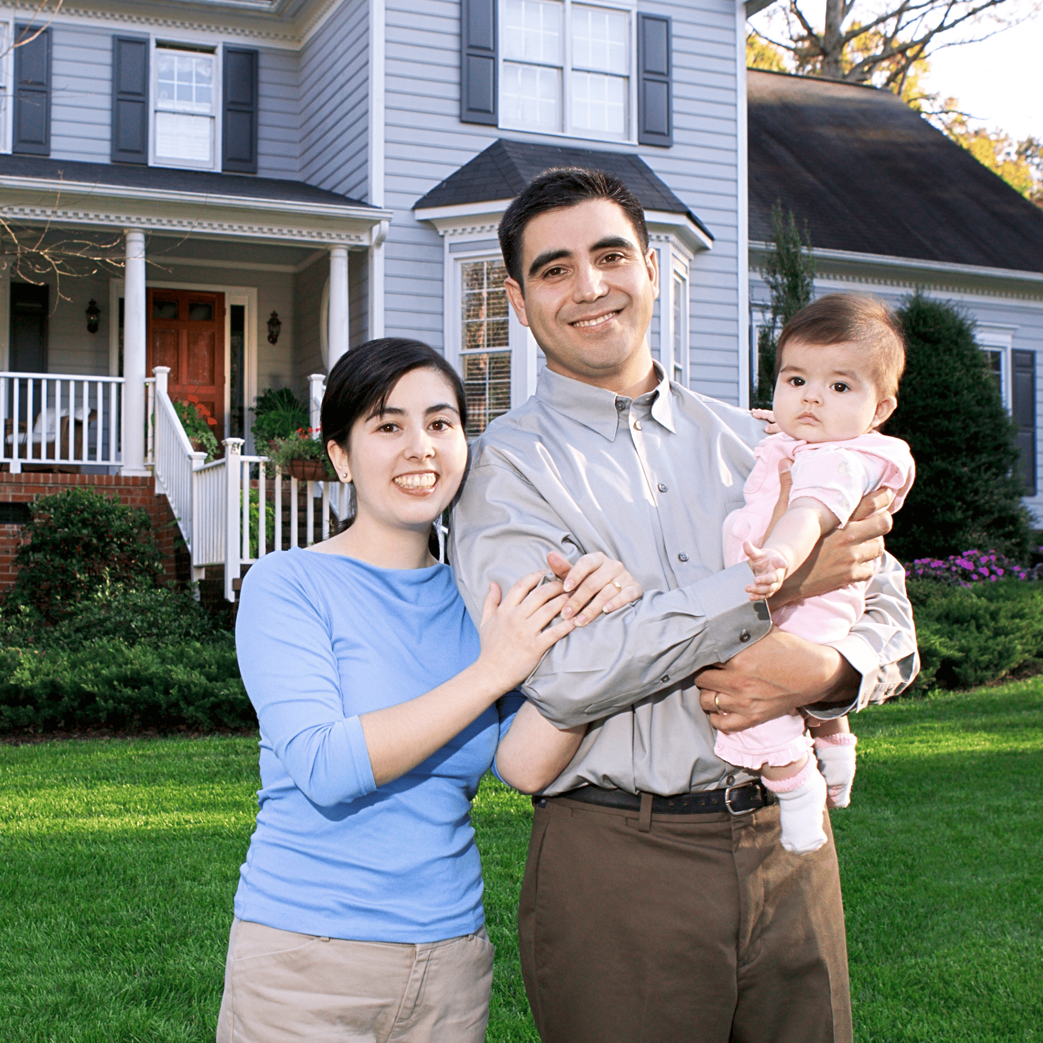 Young couple smiling while holding their baby daughter in front of their suburban home on a sunny day
