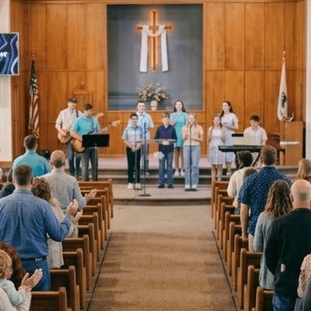team Church choir and worship band performing during Sunday service in sanctuary with wooden pews and illuminated cross